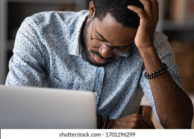 Exhausted african american male employee feel fatigue fall asleep at workplace, tired unwell biracial young man take nap sleep distracted from computer work, overwhelmed or overwork in office