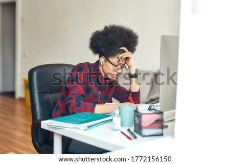 Exhausted afro american woman studying online at home. Sitting at her comfortable workplace, using computer and making some notes. Feeling tired. E-learning. Distance education. Stay home
