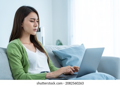 Exhausted Asian Business Woman Hurt Eye While Using Laptop Computer. Young Girl Office Worker Sit On Sofa Feel Visual Fatigue And Eye Strain Tired From Overwork And Massage Dry Irritable Eye At Home.