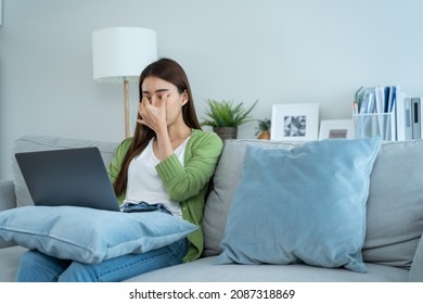 Exhausted Asian business woman hurt eye while using laptop computer. Young girl office worker sit on sofa feel visual fatigue and eye strain tired from overwork and massage dry irritable eye at home. - Shutterstock ID 2087318869