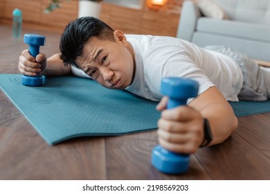 Exhausted Asian Mature Man Laying Down On Yoga Mat With Dumbbells In Hands, Sportsman Feeling Tired After Domestic Workout, Closeup