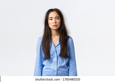 Exhausted asian woman with messy hair after lying in bed, wearing pajamas, looking tired with sleepy eyes as suffering insomnia, didnt have much sleep, waking up early, standing white background
