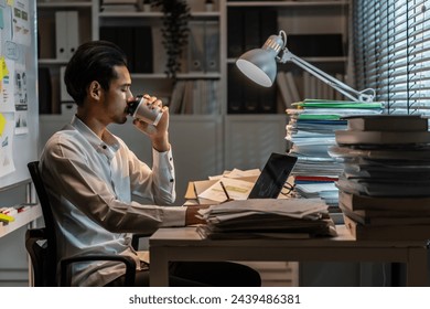 Exhausted Asian young businessman overworking late at night in office. Attractive busy male employee worker feel tired of many paper work on table and use computer plan project at corporate workplace. - Powered by Shutterstock