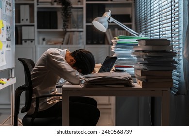 Exhausted Asian young businessman overworking late in office at night. Attractive busy man freelancer feel tired and fatigue, lying on working table and sleeping on desk in corporate workplace. - Powered by Shutterstock