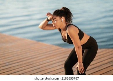 Exhausted Attractive Millennial African American Sporty Woman In Tight Black Sportswear Getting Ready For Marathon, Training Next To City Lake, Having Break, Touching Her Head, Copy Space