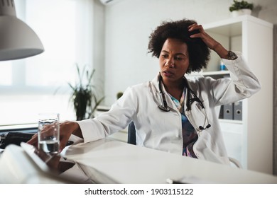 Exhausted Black Female Doctor Sits At Her Office Taking Break