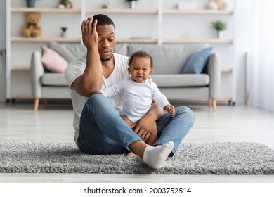 Exhausted Black Young Father Sitting With Crying Newborn Baby On Floor At Home, Desperate African American Dad Can Not Manage Upset Infant Child, Suffering Problems During Paternity Leave