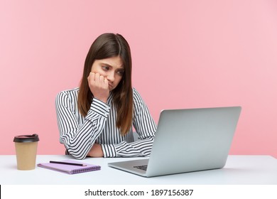 Exhausted bored woman office worker looking at laptop screen with sadness, leaning on arm, feeling lazy uninterested in her job, depression at work. Indoor studio shot isolated on pink background