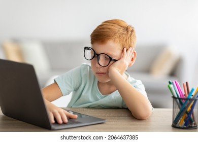 Exhausted boy feeling sleepy while doing homework for school, using notebook, copy space. Tired or bored redhead child with glasses sitting in front of computer with hand on keyboard, home interior - Powered by Shutterstock