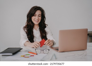 Exhausted Brunette Woman In White Shirt And Violet Pants Sitting On Sofa, Holding Phone Hiding Her Face By Hand, Ashamed, Tired After Hard Discussion Via Video Call. Woman Received Bad News By Phone.