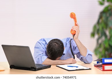 Exhausted businessman with face down holding a telephone in an office