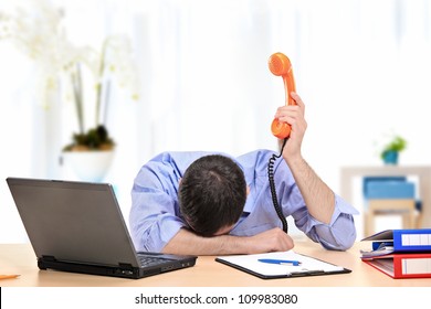 An exhausted businessman holding a telephone in his office