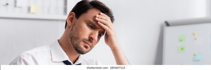 Exhausted businessman with migraine holding hand on forehead, while looking away on blurred background, banner - Shutterstock ID 1855697113