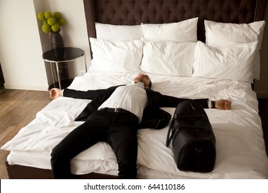 Exhausted Businessman Resting On Bed After Long Air Flight, Jet Lag. Man In Business Suit Lying With Arms Outstretched On Mattress In Hotel Room. Happy Buyer Sleeping In New Comfortable House Room