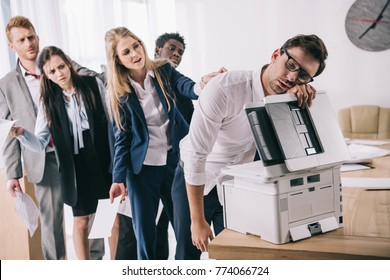 exhausted businessman sleeping on copier while his colleagues standing in queue behind him