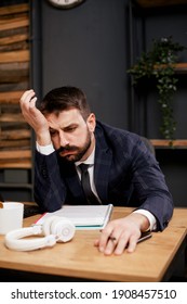 Exhausted businessman working on computer in the office. Tired man sitting at office desk drinking coffee.