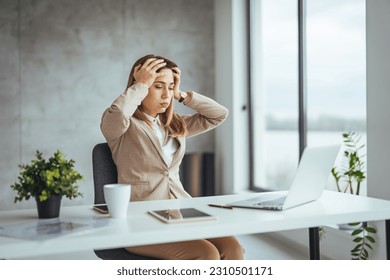 Exhausted businesswoman having a headache in modern office. Mature creative woman working at office desk with spectacles on head feeling tired. Stressed casual business woman feeling eye pain  - Shutterstock ID 2310501171