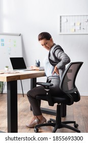 Exhausted Businesswoman With Hurting Back Holding Hand On Hip, While Sitting On Office Chair In Office