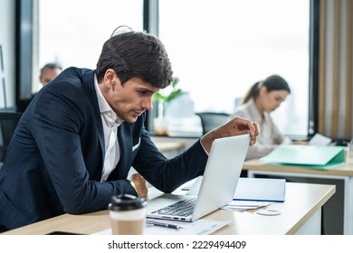 Exhausted Caucasian businessman using laptop computer work in office. Young employee male worker sitting on table feel sleepy and yawning tired from overwork job and drinking hot coffee in workplace. - Shutterstock ID 2229494409