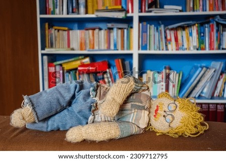 Exhausted Crocheted Male Engineer Doll: Blond Curls, Mustache, Plaid Shirt, and Glasses - Ingenious Concept Image of a Fatigued Man Resting by a Lower Bookshelf ! Learning struggles concept image .