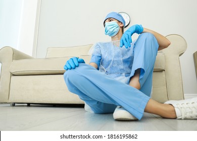 Exhausted Doctor Sitting On Floor Indoors, Low Angle View. Stress Of Health Care Workers During COVID-19 Pandemic