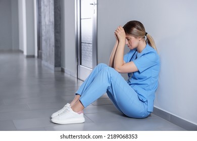 Exhausted Doctor Sitting On Floor In Hospital, Space For Text