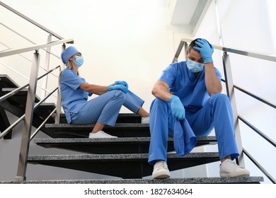 Exhausted Doctors Sitting On Stairs Indoors. Stress Of Health Care Workers During COVID-19 Pandemic