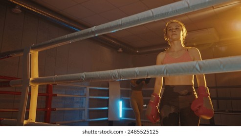 Exhausted female boxer returns to corner of a vividly lit boxing ring after intense sparring session, capturing her fatigue and determination - Powered by Shutterstock