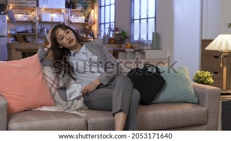 exhausted female manager arriving home. putting down her briefcase and slumping in sofa. sitting cross legged and letting out heavy sigh. genuine lifestyle