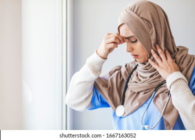 Exhausted Female Muslim Doctor Taking A Break. Shot Of A Young Female Nurse Looking Stressed Out While Standing At A Window In A Hospital. It's A Stressful Profession