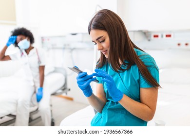 An exhausted female nurse and a african american doctor sits on a bed in a hospital during a shift break. She daydreams while holding his smartphone. - Powered by Shutterstock