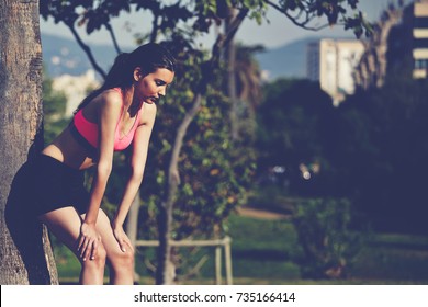Exhausted female taking break in the park after training. Young woman sportsman rest during workout