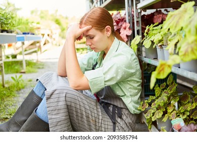 Exhausted and frustrated young woman as a gardener in front of the nursery greenhouse