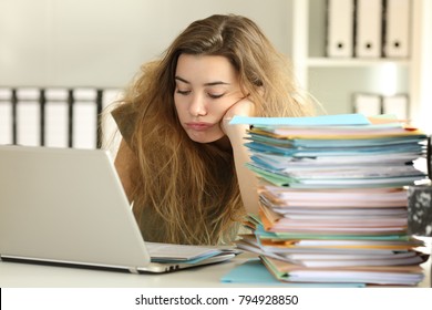 Exhausted intern with tousled hair working hard reading a lot of documents at office 