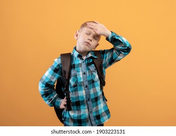 Exhausted Kid Schooler With Heavy Backpack Touching His Forehead On Yellow Studio Background. Tired Redhead Boy In Plaids Shirt Got Tired Of Studying, Suffering From Burnout In School