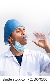 Exhausted Latino Male Nurse, Drinking Water From A Disposable Bottle. Hispanic Person On White Background.