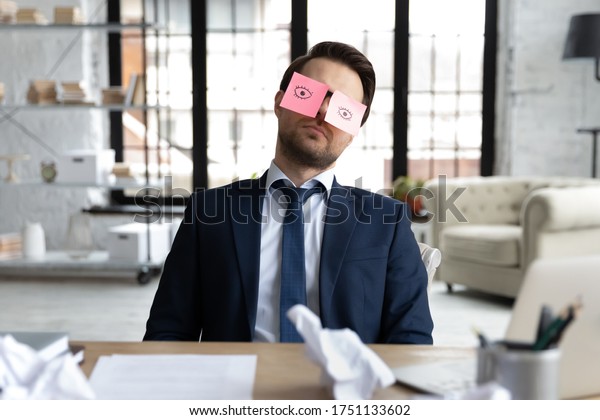 Exhausted male employee sit at desk with stickers\
on eyes fall asleep nap at workplace, tired businessman or boss\
sleeping in office, overwhelmed with work, feel fatigue exhaustion,\
overwork concept