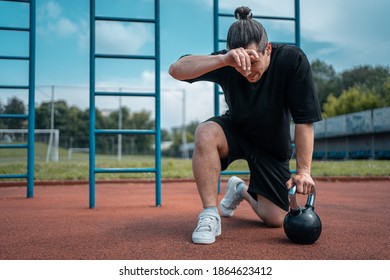 exhausted man athlete taking break between exercising with kettlebell outdoor