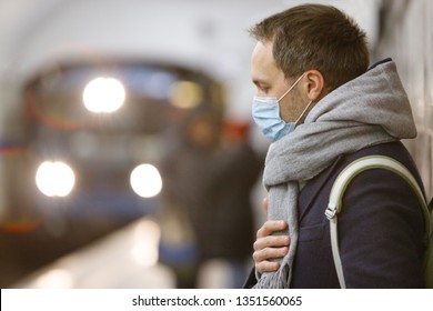 Exhausted Man Feeling Sick, Wearing Protective Mask Against Transmissible Infectious Diseases And As Protection Against The Flu In Public Transport/subway, Train And People On Background, Soft Focus. 