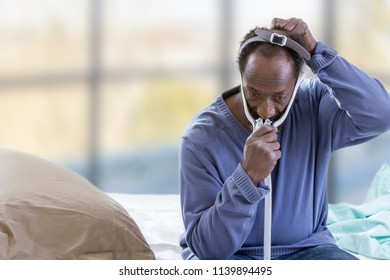 Exhausted Man With Sleep Apnea Using CPAP Machine, Wearing Headgear Mask Connecting To Air Tube