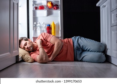 exhausted man sleeping on floor in kitchen near open refrigerator 