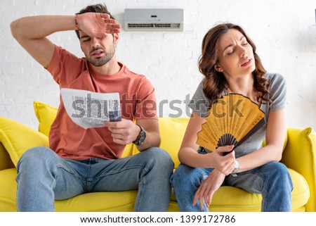 exhausted man and woman sitting on sofa and suffering from heat at home
