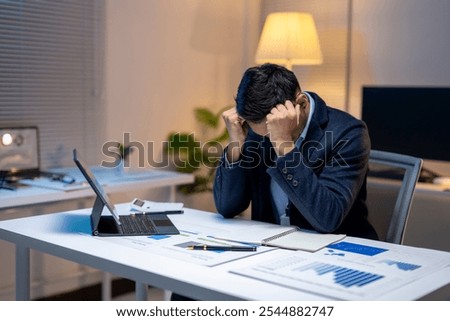 Exhausted manager having a headache while analyzing marketing reports and financial charts on laptop, working until late at night in office