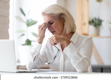 Exhausted Mature Female Employee Sit At Desk Take Off Glasses Massage Eyes Suffer From Headache Migraine, Tired Middle-aged Businesswoman Have Dizziness Or Blurry Vision, Health Problem Concept