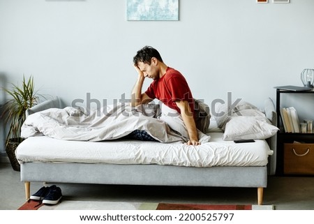 Exhausted mature man waking up in the morning, he sitting on bed and rubbing his eyes
