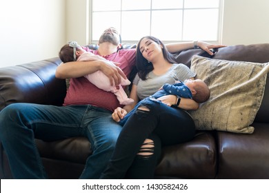 Exhausted Mid Adult Parents Carrying Sleeping Babies While Resting On Sofa