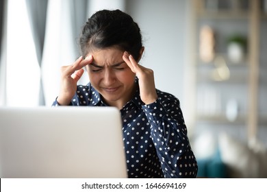 Exhausted millennial Indian girl touch massage temples suffer from headache or migraines, tired young ethnic woman overwhelmed with computer work, struggle with dizziness, health problem concept