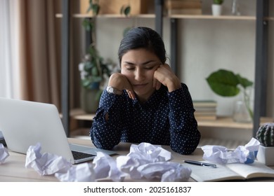 Exhausted millennial Indian woman sit at desk at home office fall asleep try to meet deadline. Tired young biracial female work on computer sleep or take nap at workplace. Fatigue, exhaustion concept.