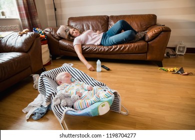 Exhausted Mother Having A Nap On The Sofa While Her Newborn Child Has A Sleep.