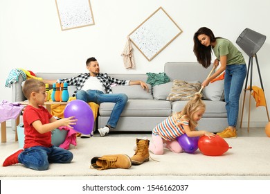 Exhausted mother trying to clean up mess made by children and lazy father in room - Shutterstock ID 1546162037